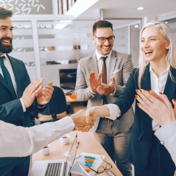 Business partners shaking hands while other colleagues clapping. Boardroom interior. Successful leaders have the courage to take action where others hesitate.