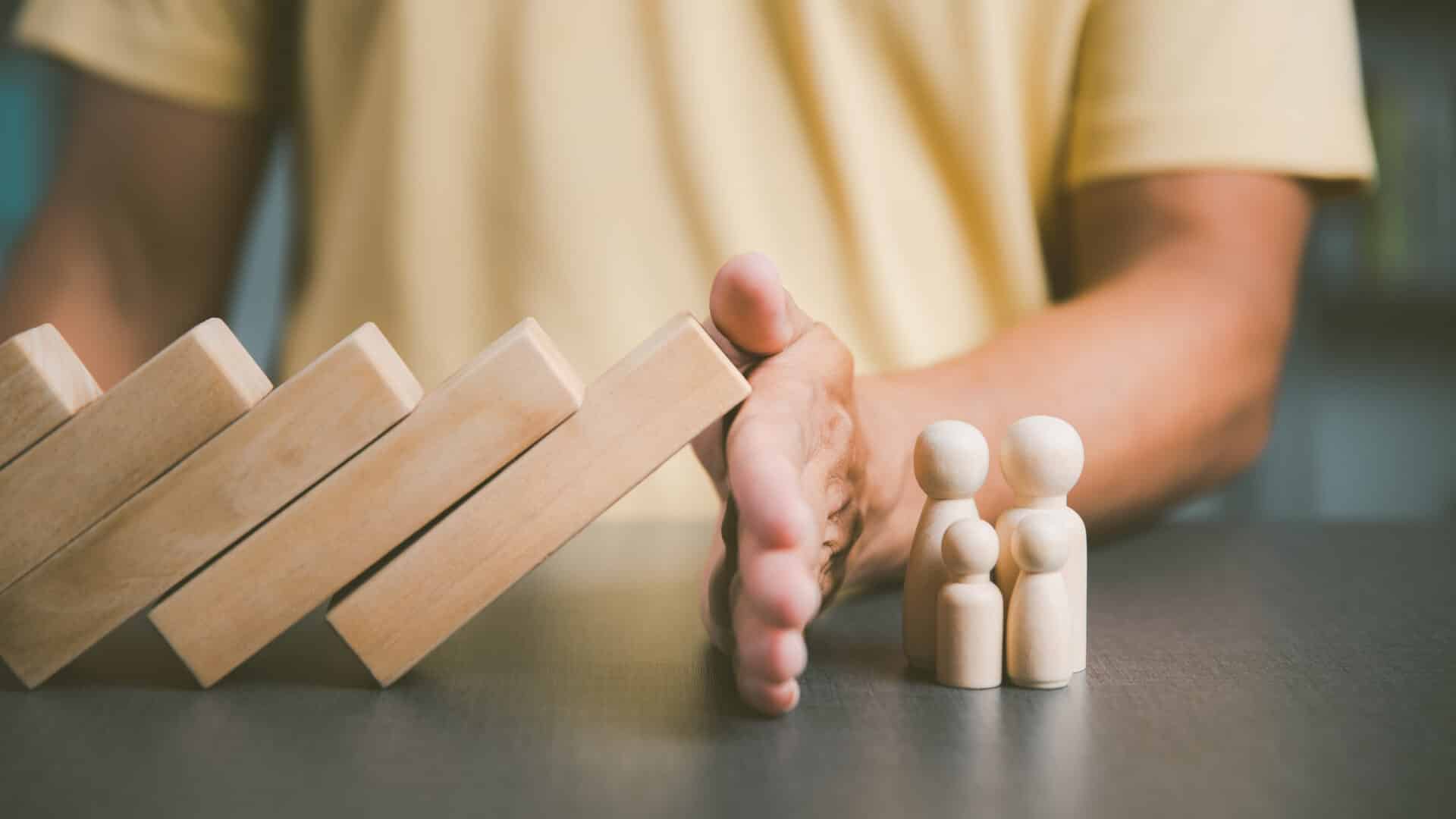 Father blocked the wooden block with his hand to show protection for the family. and support and help with advice The concept of family relationships that will connect to safety love and compassion