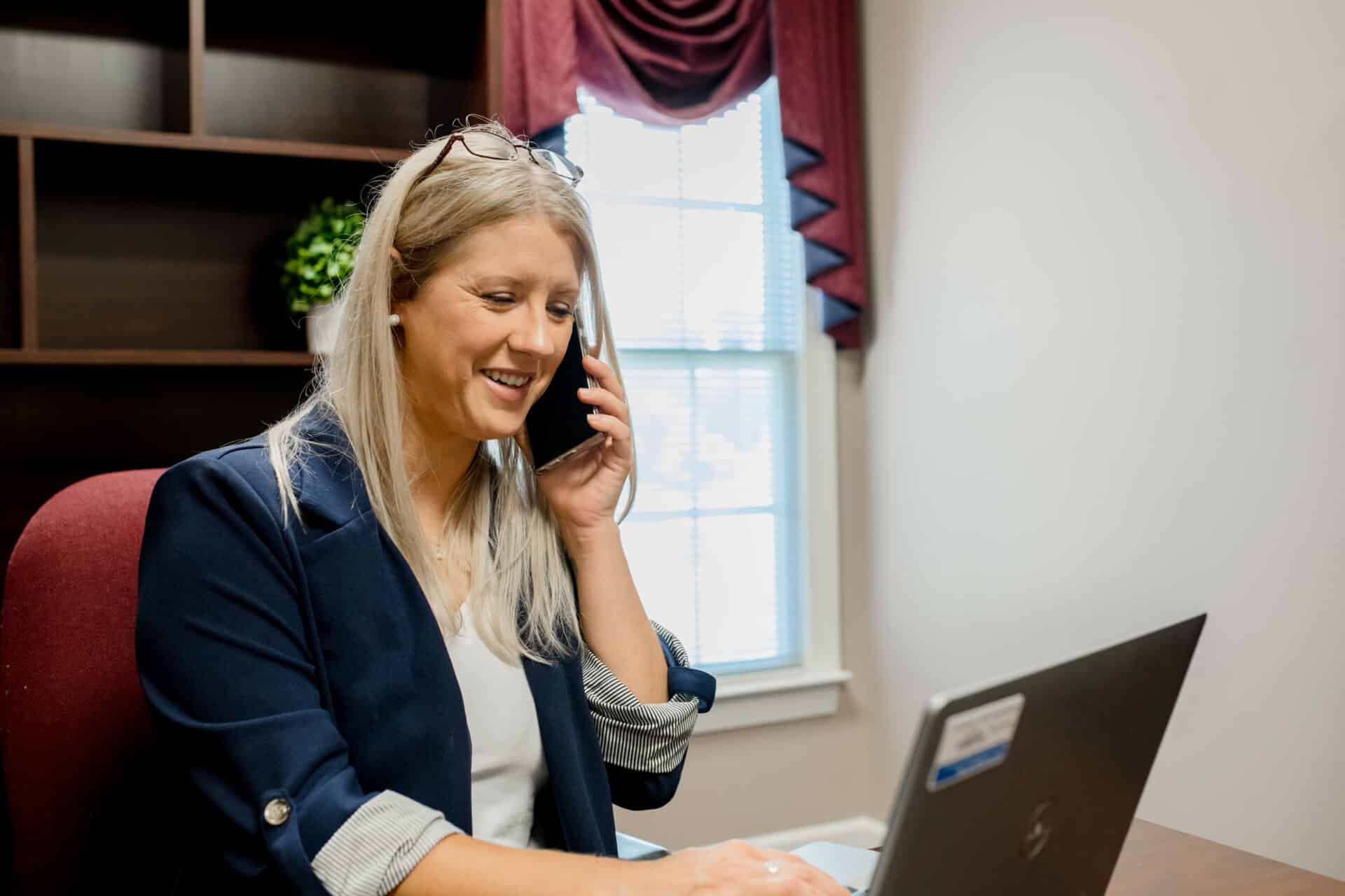 woman talking on the phone while typing on her laptop in her office