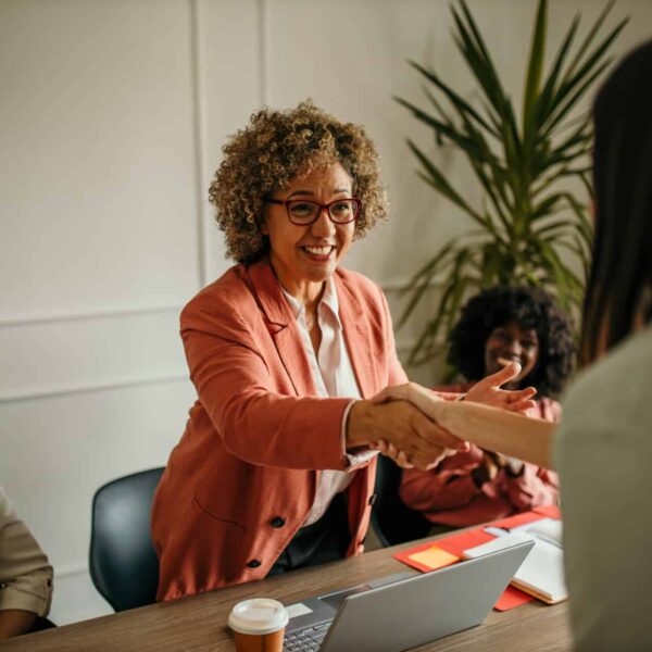 Smiling mature female executive making a successful deal with partner shaking hand at work standing at meeting table