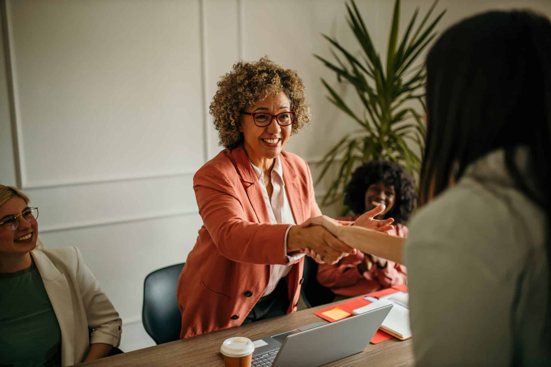 Smiling mature female executive making a successful deal with partner shaking hand at work standing at meeting table