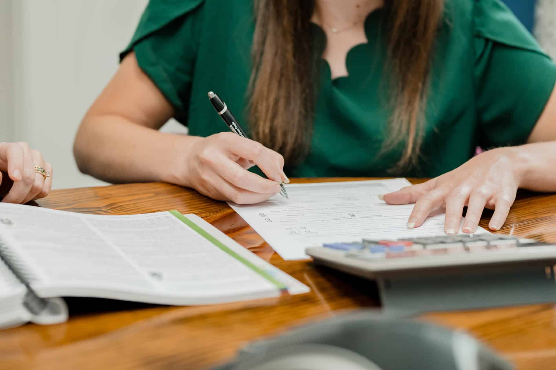 woman filling out form in front of a desk calculator