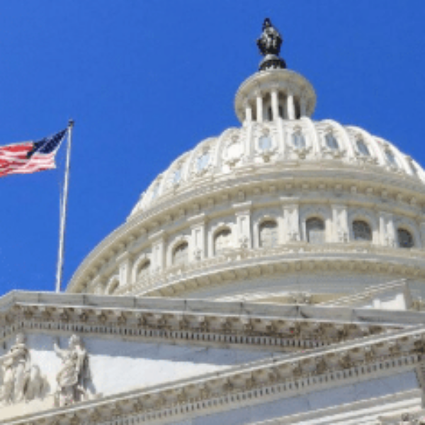 The dome of the United States Capitol building with a statue on top, an American flag waving, and a bright blue sky in the background.